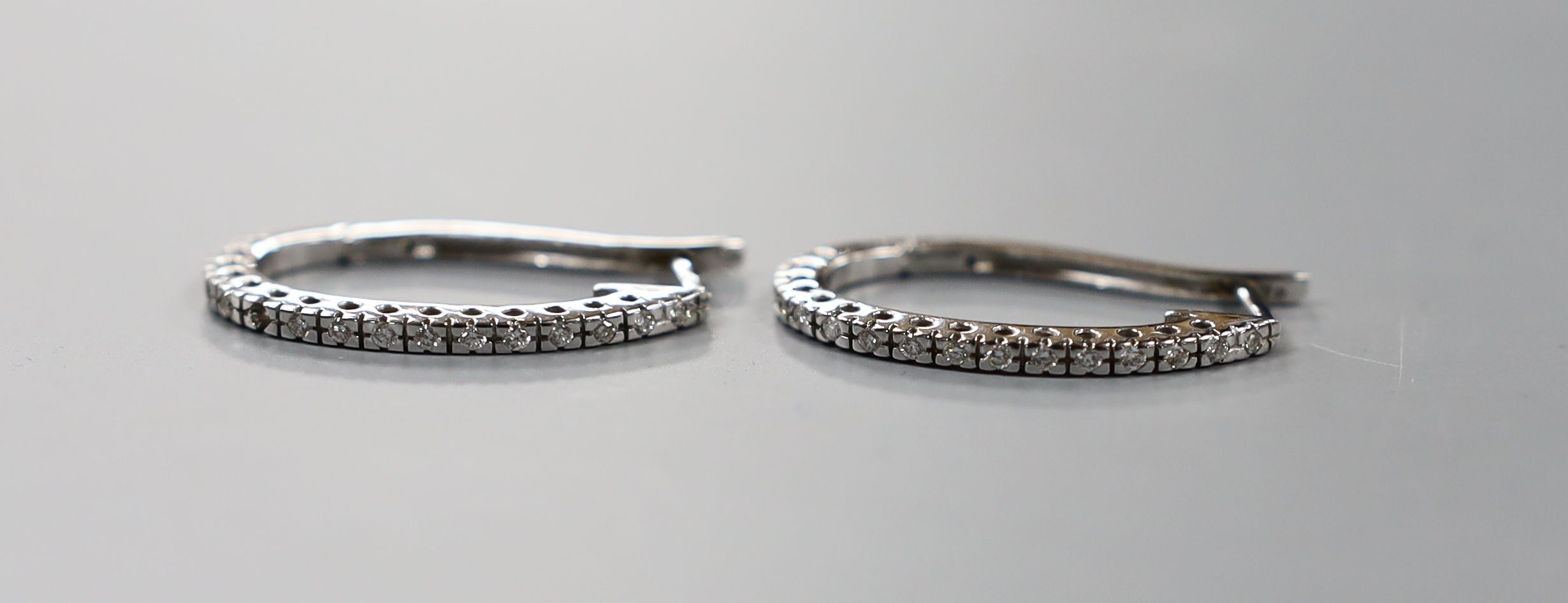 A pair of modern white metal and diamond chip set half hoop earrings, 27mm,gross weight 5.9 grams.